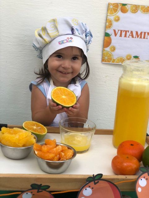 Aluna com chapéu de chef segurando uma laranja