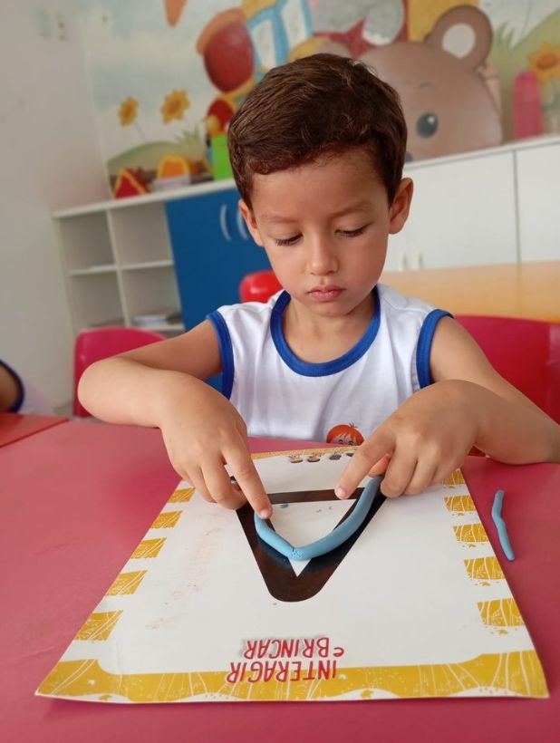 Aluno modelando massinha sobre a letra V